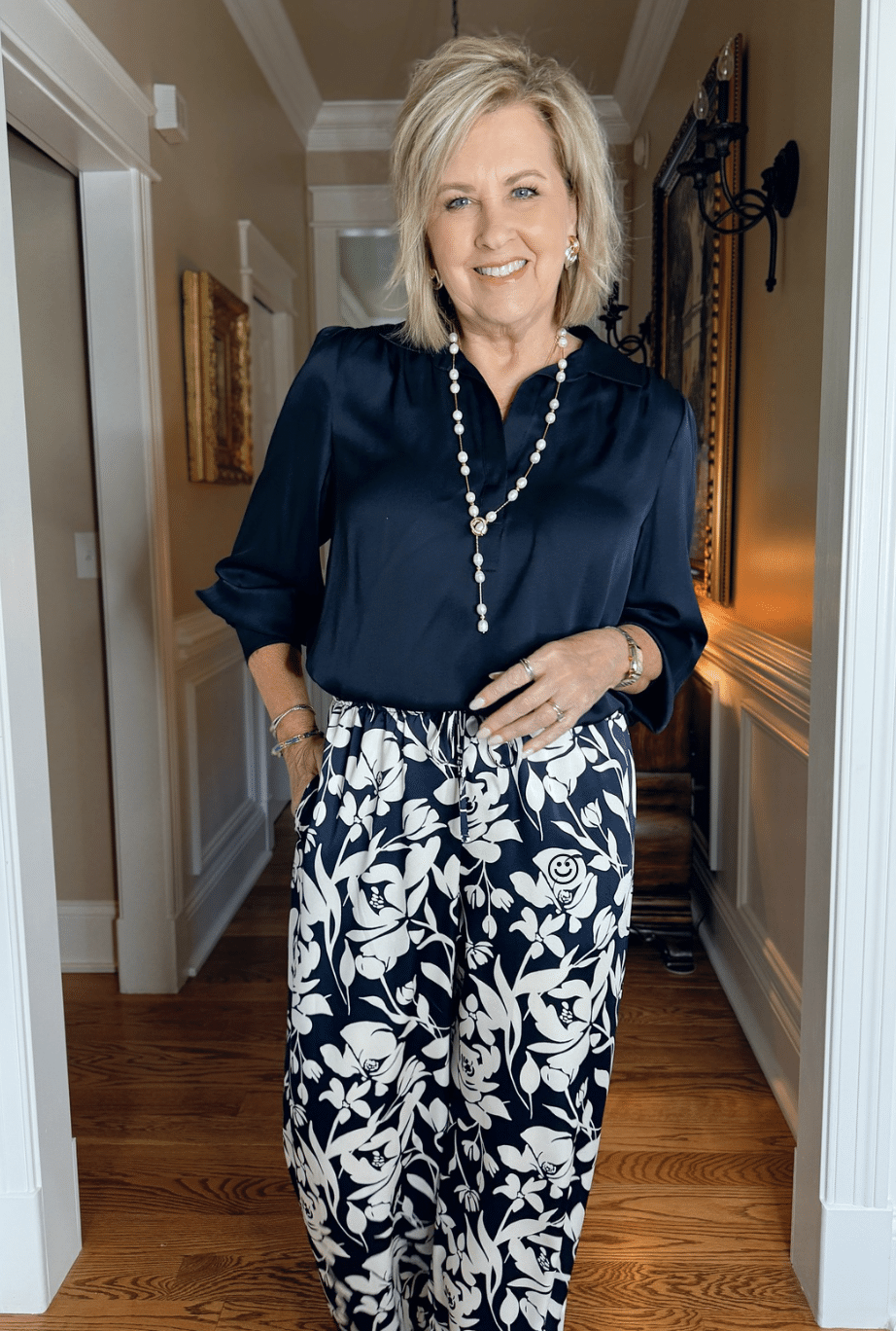 Woman wearing floral satin wide-leg pants from Target and a navy washable silk blouse with a pearl necklace